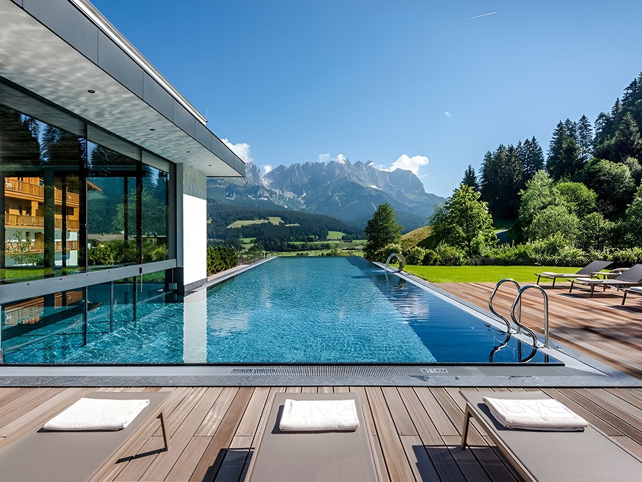 Πισίνα με φόντο βουνό και ξαπλώστρες σε δροσερό φυσικό περιβάλλον
